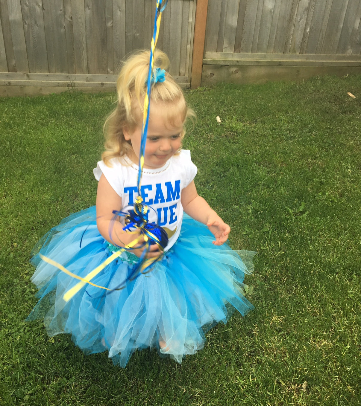 Child in a blue and yellow costume with 'Team Blue' text on grass