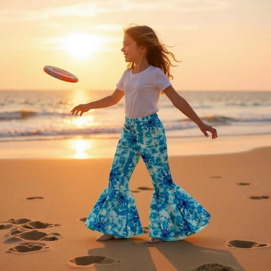 Girl wearing blue circle bellbottoms and playing with a frisbee on a beach at sunset