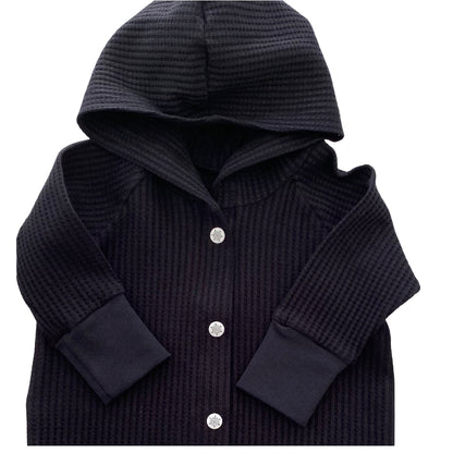 Combishort réglisse noir en tricot gaufré, barboteuse une pièce à capuche avec boutons-pression sur le devant et manches longues raglan